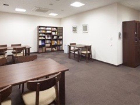 こげ茶のカーペットが格子上に敷かれたシックな色合いの部屋である。部屋の隅には本棚がある。室内には机と椅子が並んで置かれている。