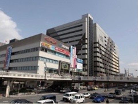 高架状の通路の向こうには巨大な建物が２棟並んでいる。高架の下は大きな道路が通っていて、たくさんの車が走っている。