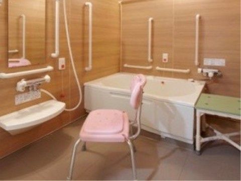 壁が木目調でスタイリッシュなデザインの浴室である。浴槽回りなど各所に手すりが設置されている。シャワーチェアも置いてある。