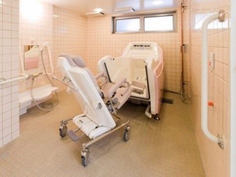 全体に白いタイルが敷き詰められた清潔感のある浴室。座ったままでも入浴できるタイプの介護浴槽が設置されている。