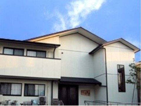 白い外壁の２階建ての建物の入口には黒い屋根がある。入口の自動ドアの横には当施設の表札が取り付けられている。
