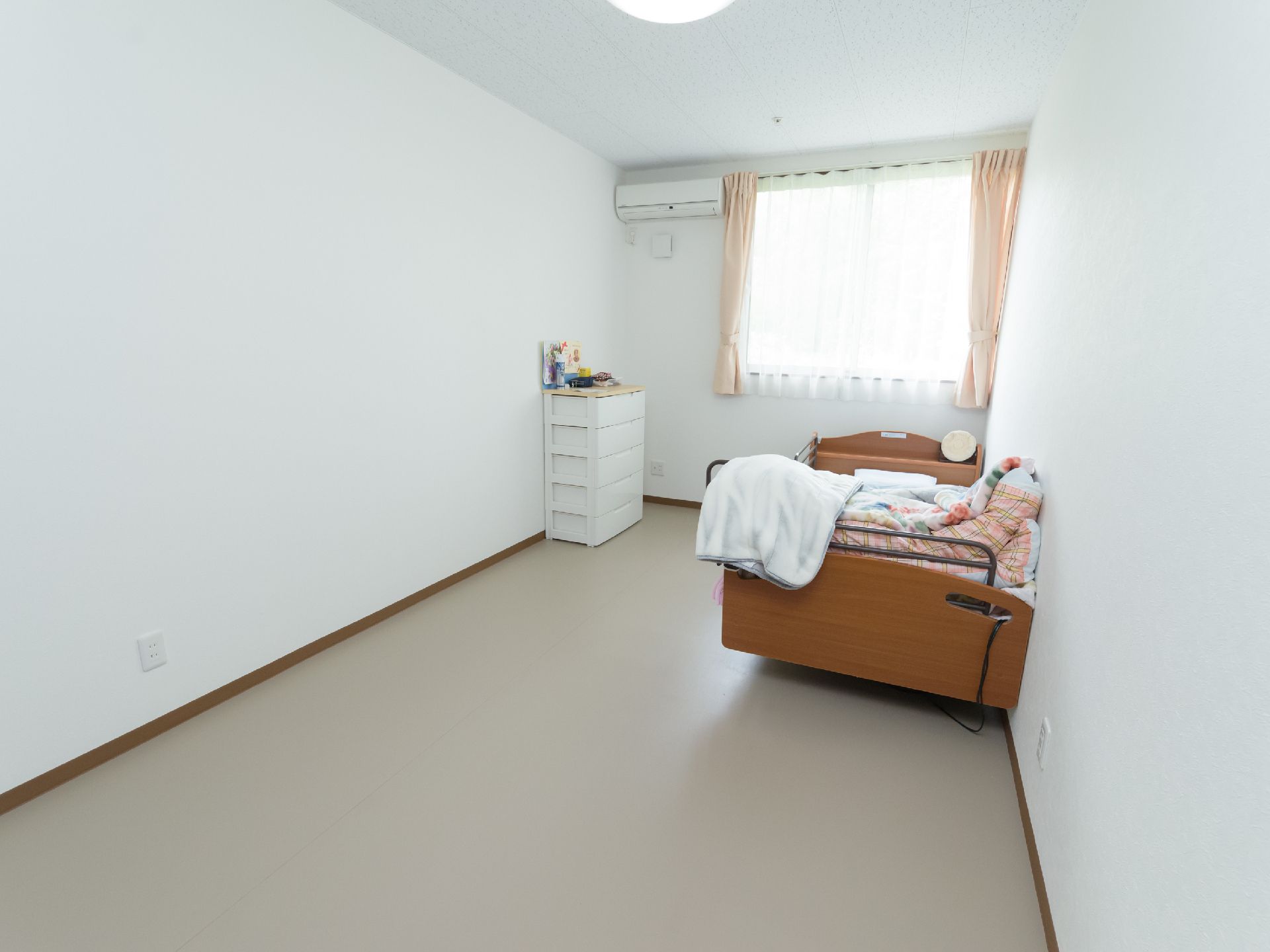 布団がかけられている介護用ベッドが壁際に置かれた居室