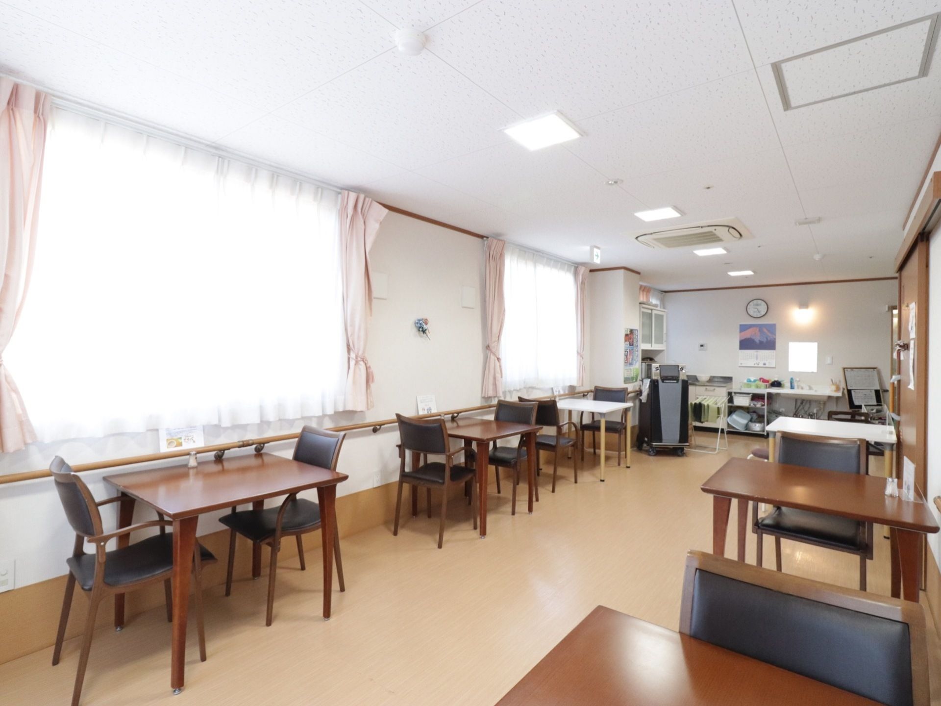 広々とした共有スペースには２人掛けのテーブルと椅子があちこちに配置されている。壁一面に手すりが設けられている。