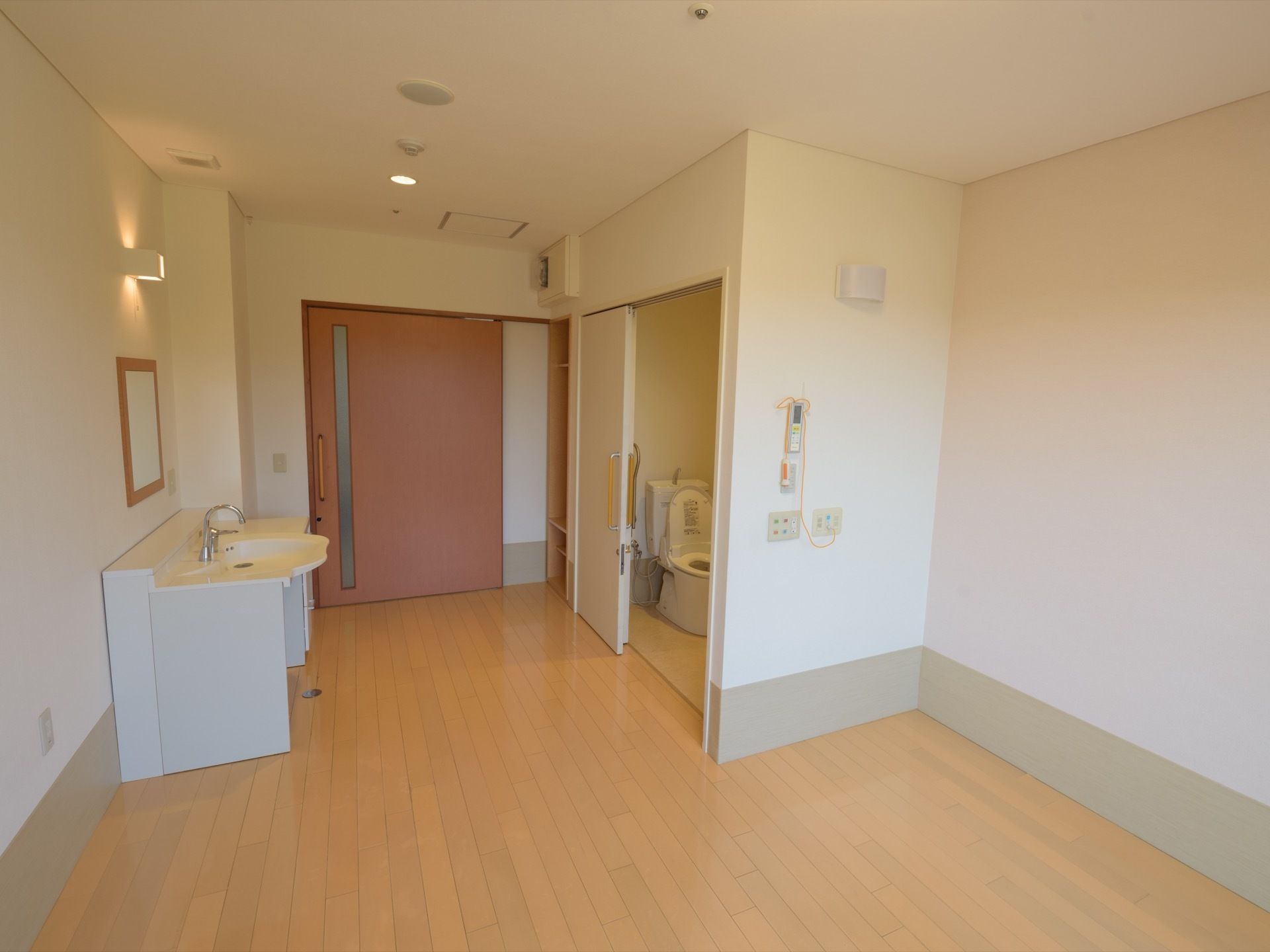 居室の扉には縦方向のスリットが入っているので、自然光が入ってくる。右手の壁際には、介護ベッドを備えることができる。複数の照明が付いている。