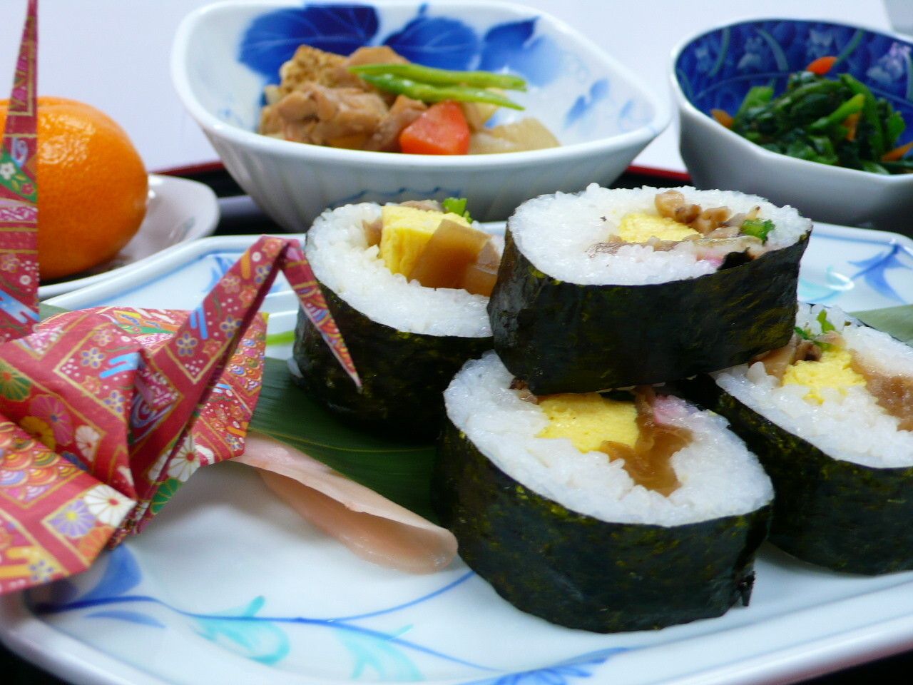 太巻き寿司と野菜の煮物やほうれん草のおひたし、デザートのみかんが付いたメニュー