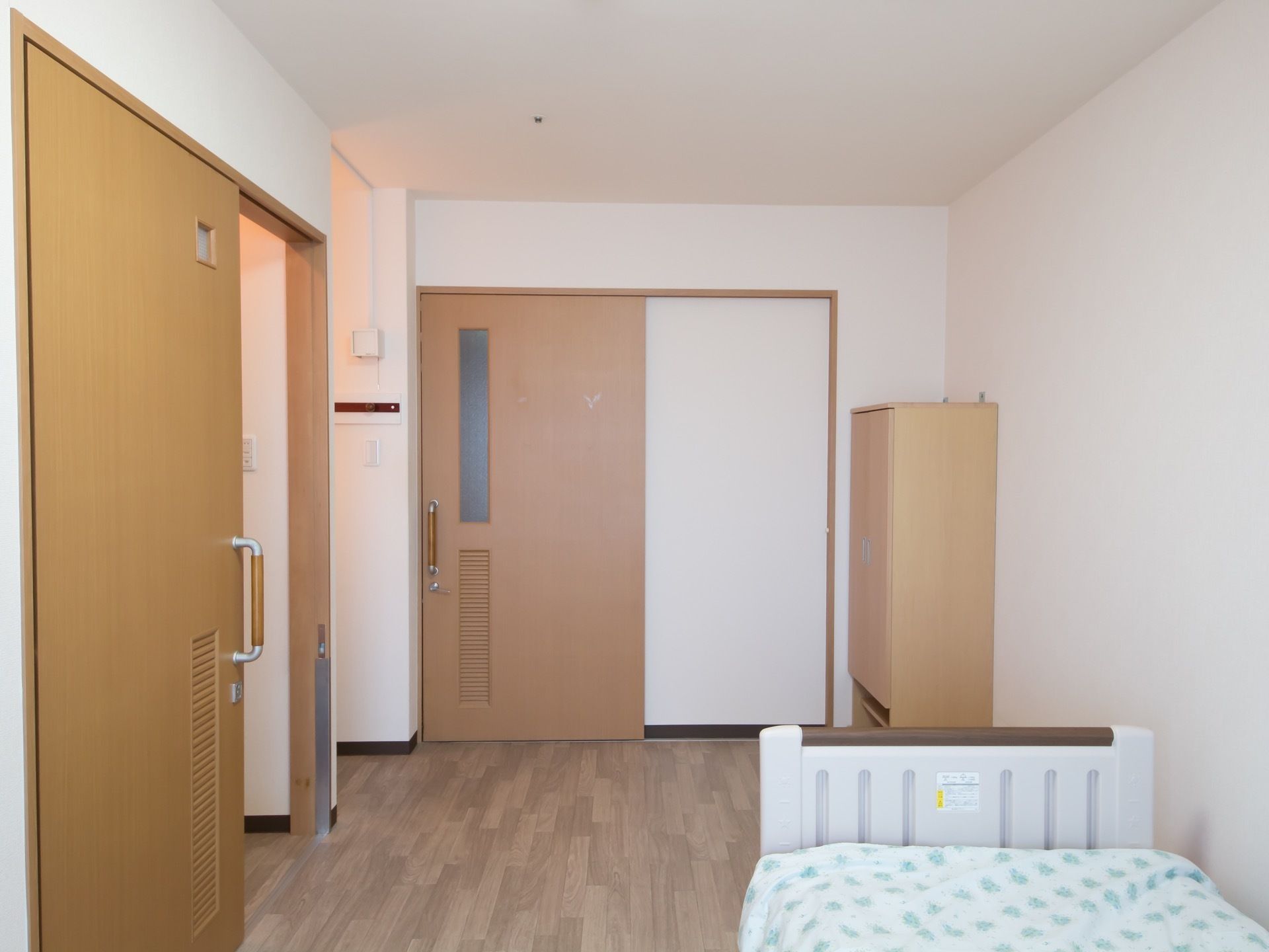 落ち着いた木目調のフローリング部屋である。扉はすべて引き戸式を採用。収納家具やベッドが設置されている。