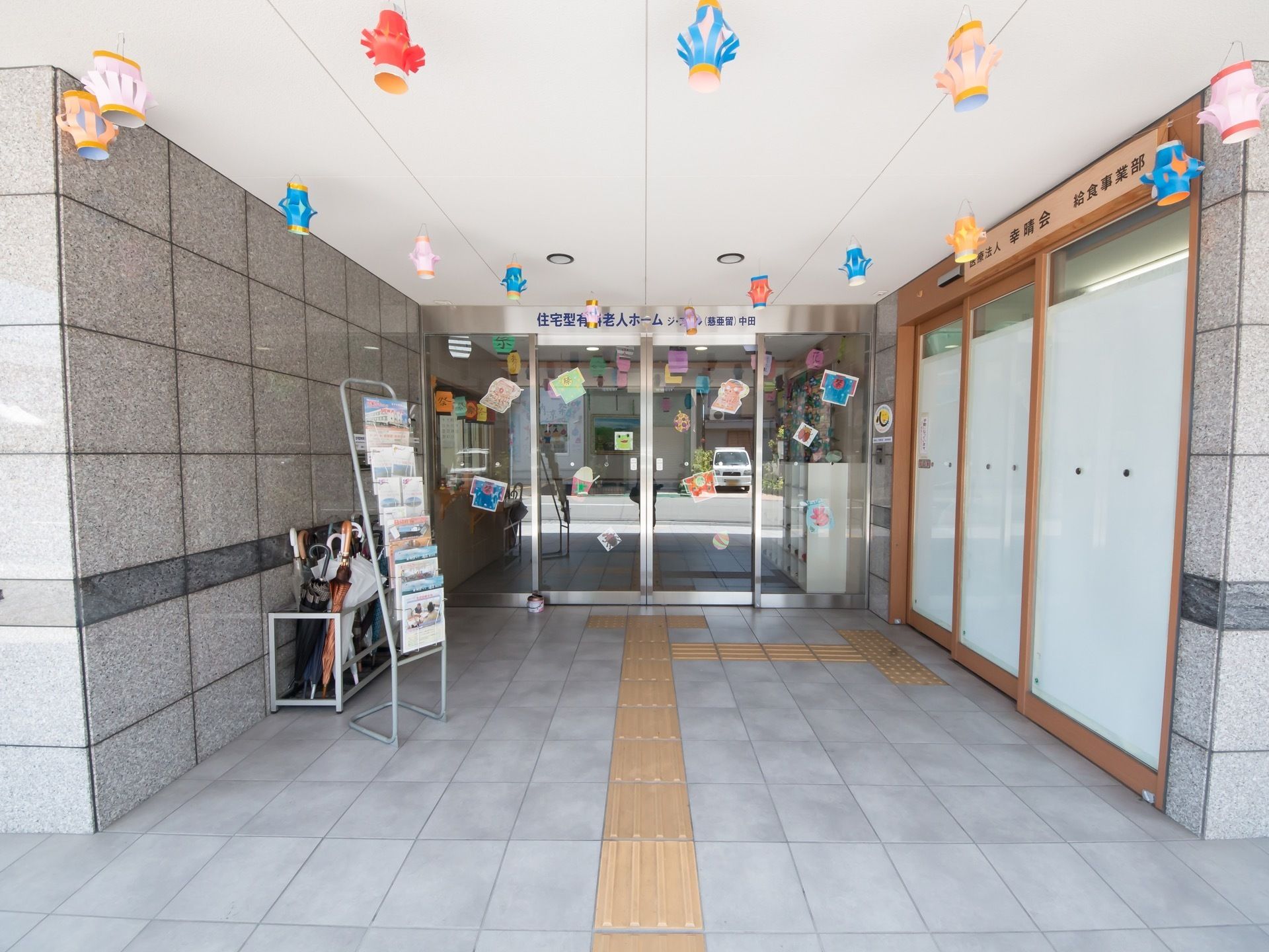 色紙で作られたカラフルな装飾物が、天井から吊り下げられている。黄色い点字ブロックが、自動ドアの前まで設置されている。