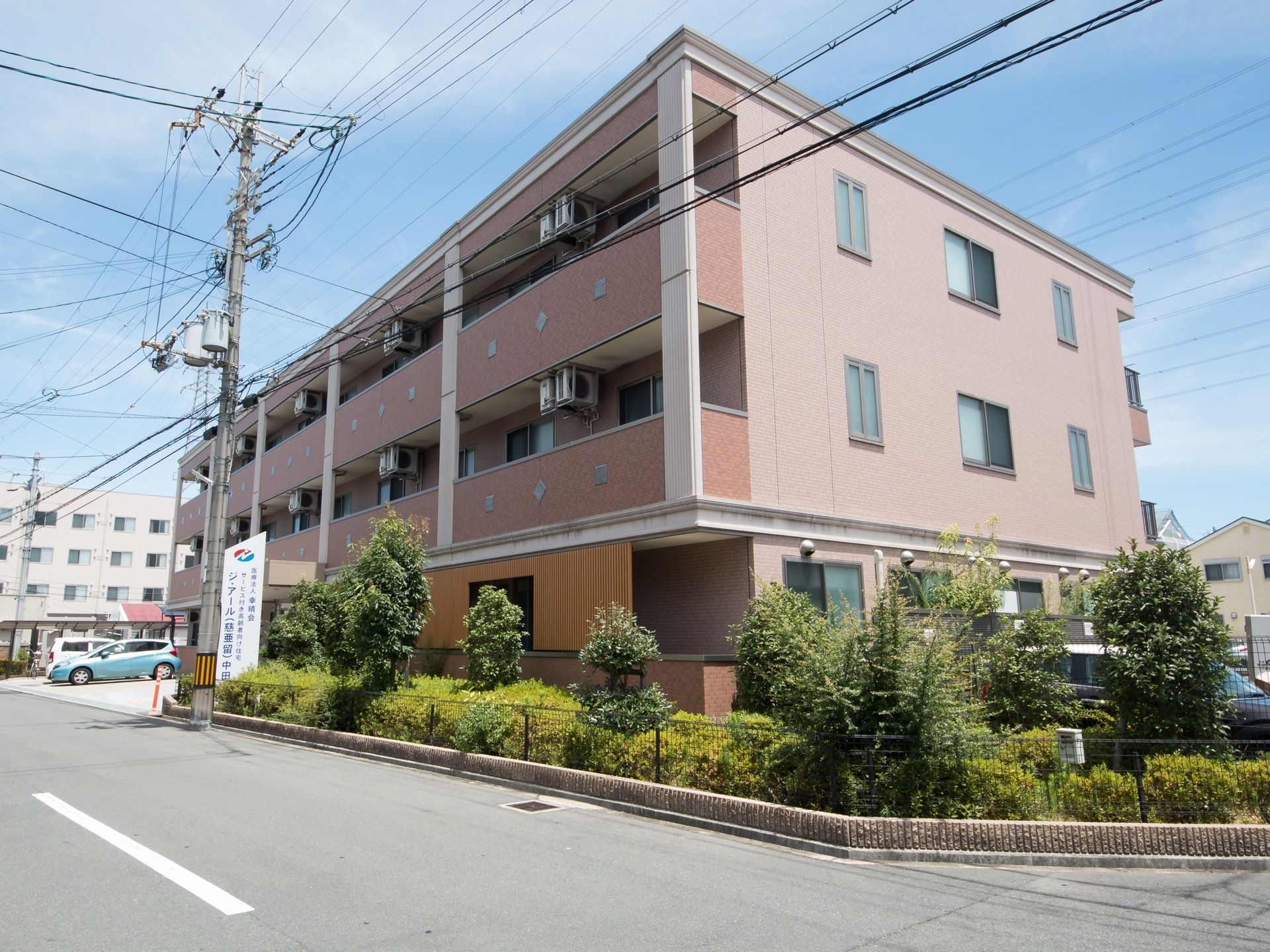 地上３階建ての施設を取り囲むように、緑の草木が植えてある。バルコニー部分の外壁は、レンガ色のデザインである。
