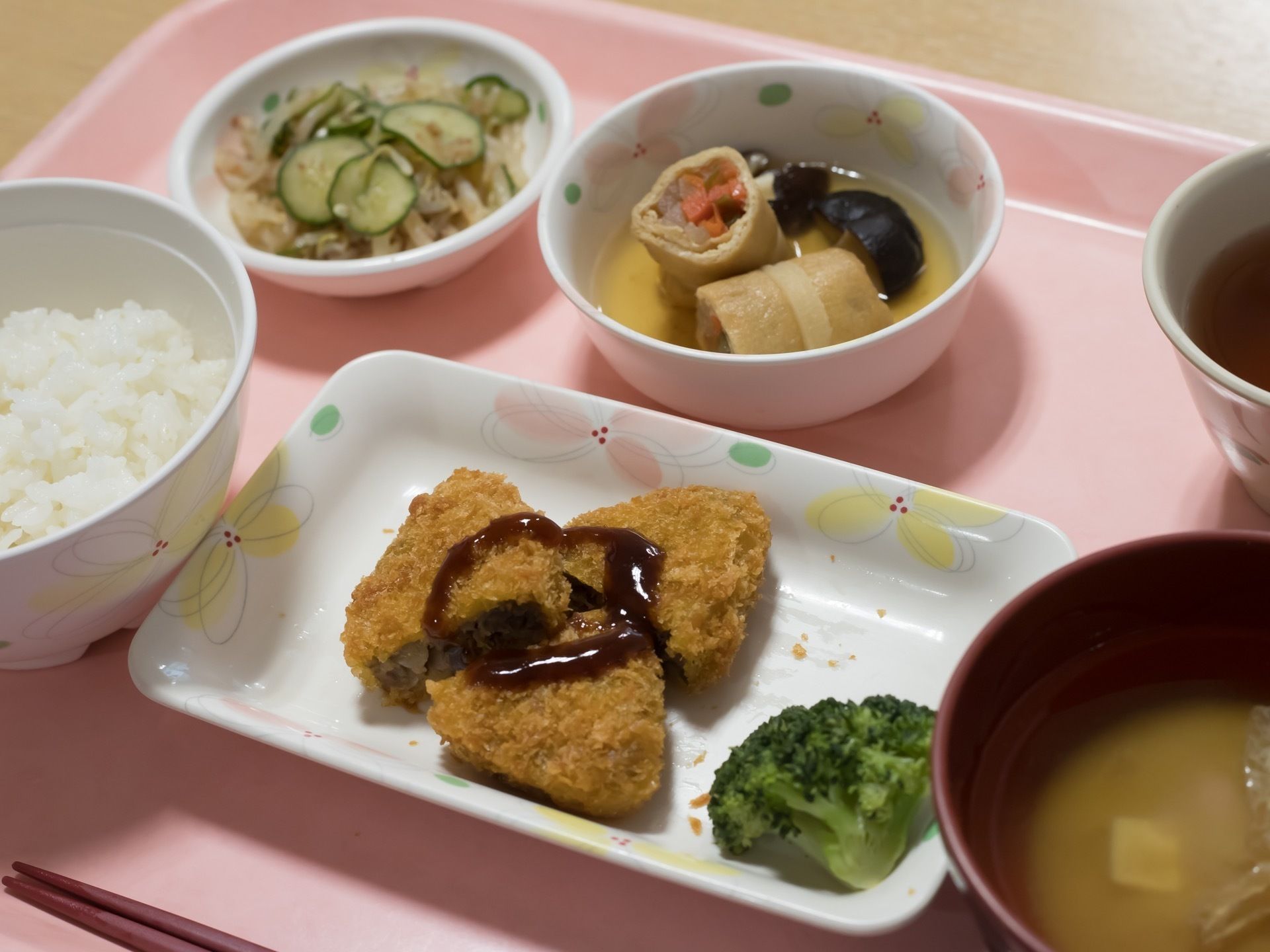 メインメニューは揚げ物である。その周りに、白米、お味噌汁、油あげと野菜の煮物、キュウリの和え物などが並んでいる。