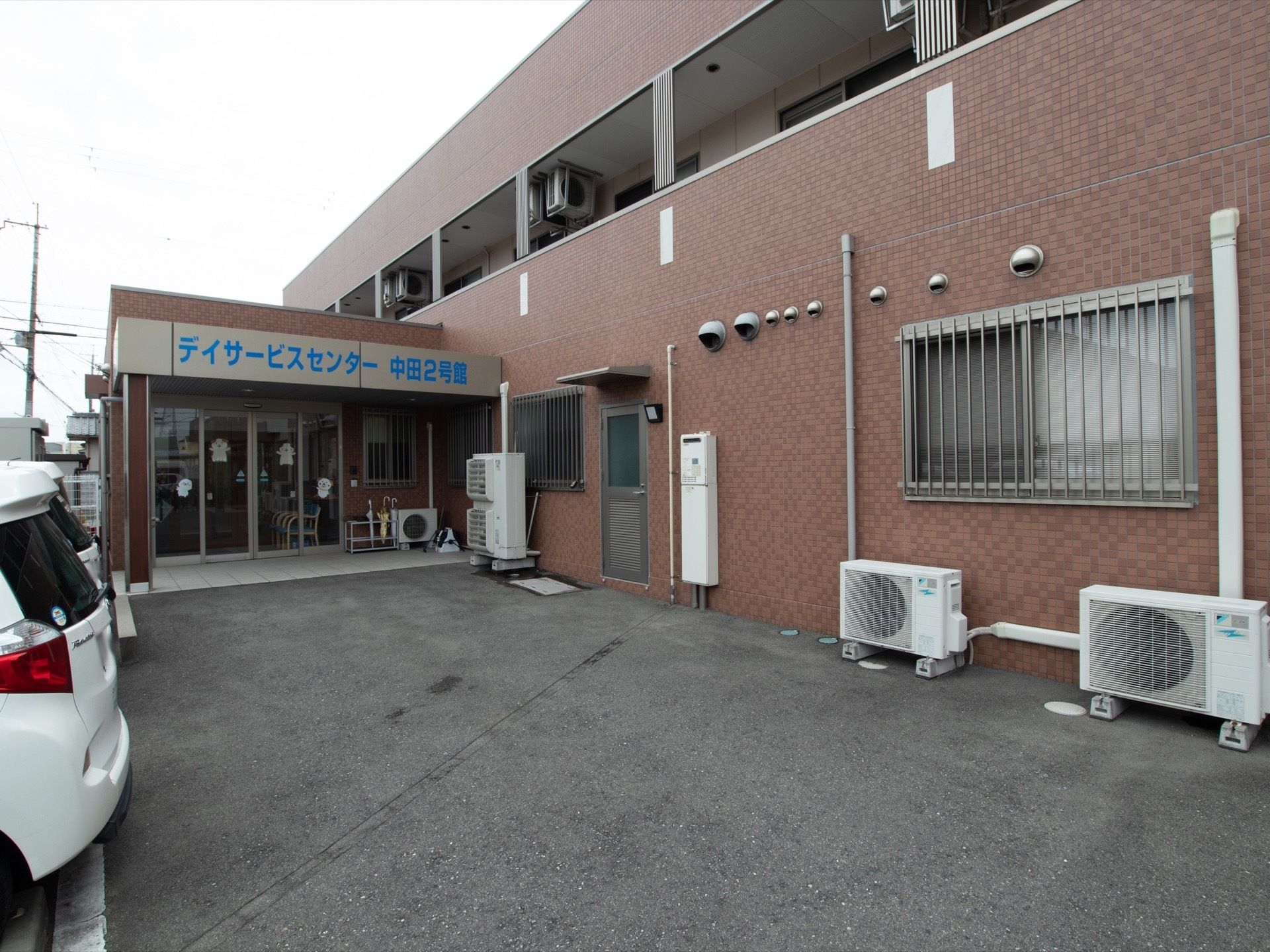 自動ドアが備わっている玄関の前にあるスペースには屋根が設けられ、傘立てが置かれている。ドアを入ると椅子が置かれている。