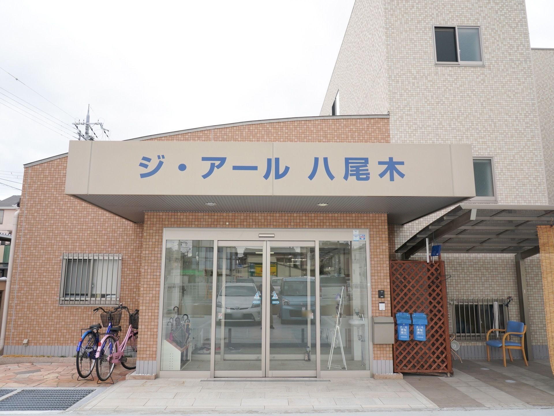 3階建ての鉄筋コンクリート造の建物で、壁面に大きな文字で施設名が書かれている。ドアの左側が駐輪場になっている。