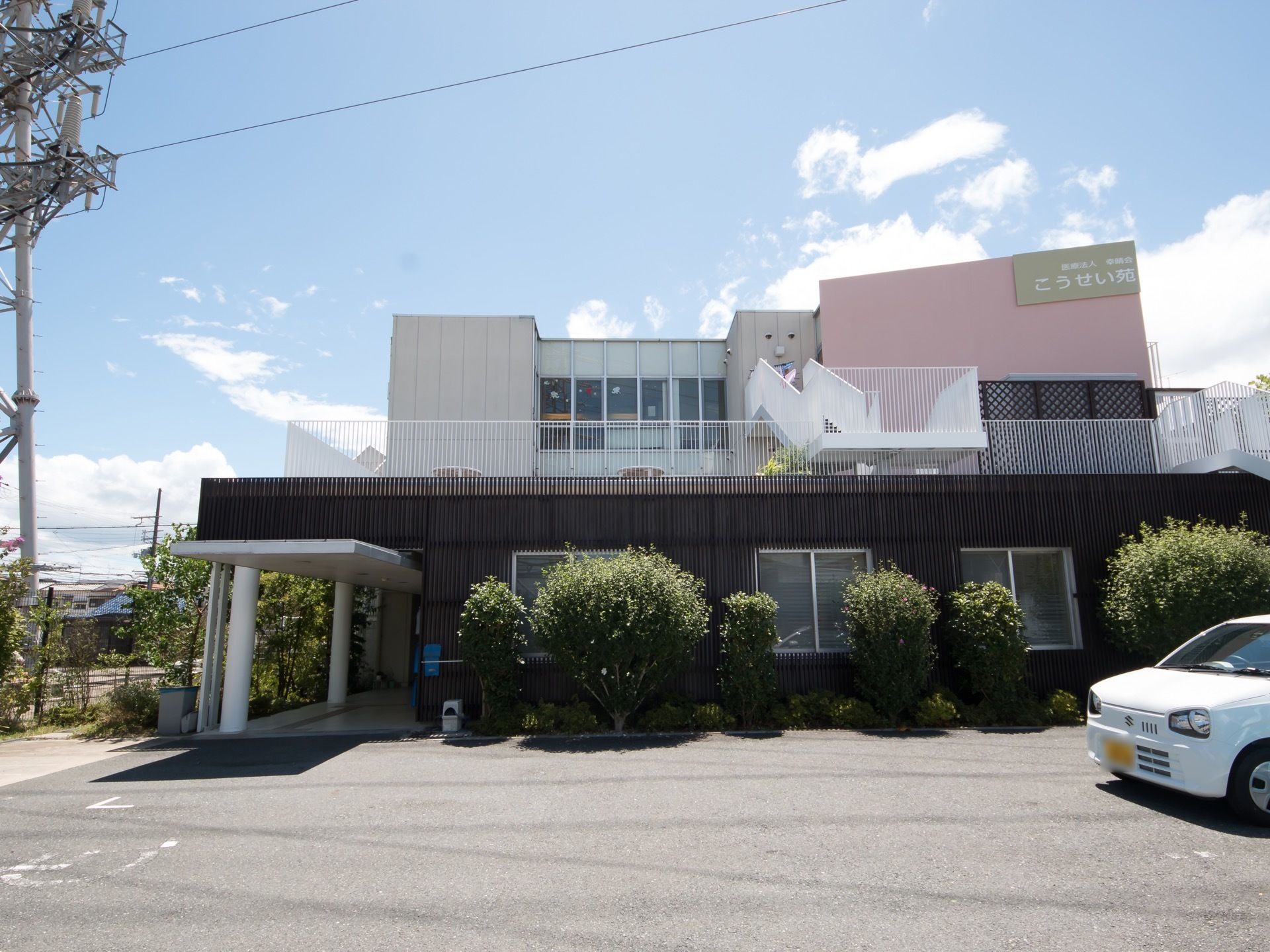 施設建物は３階建てで、ピンクの外壁部分に施設名が書かれた大きい看板が掲げられている。玄関口にはひさしが取りつけられている。