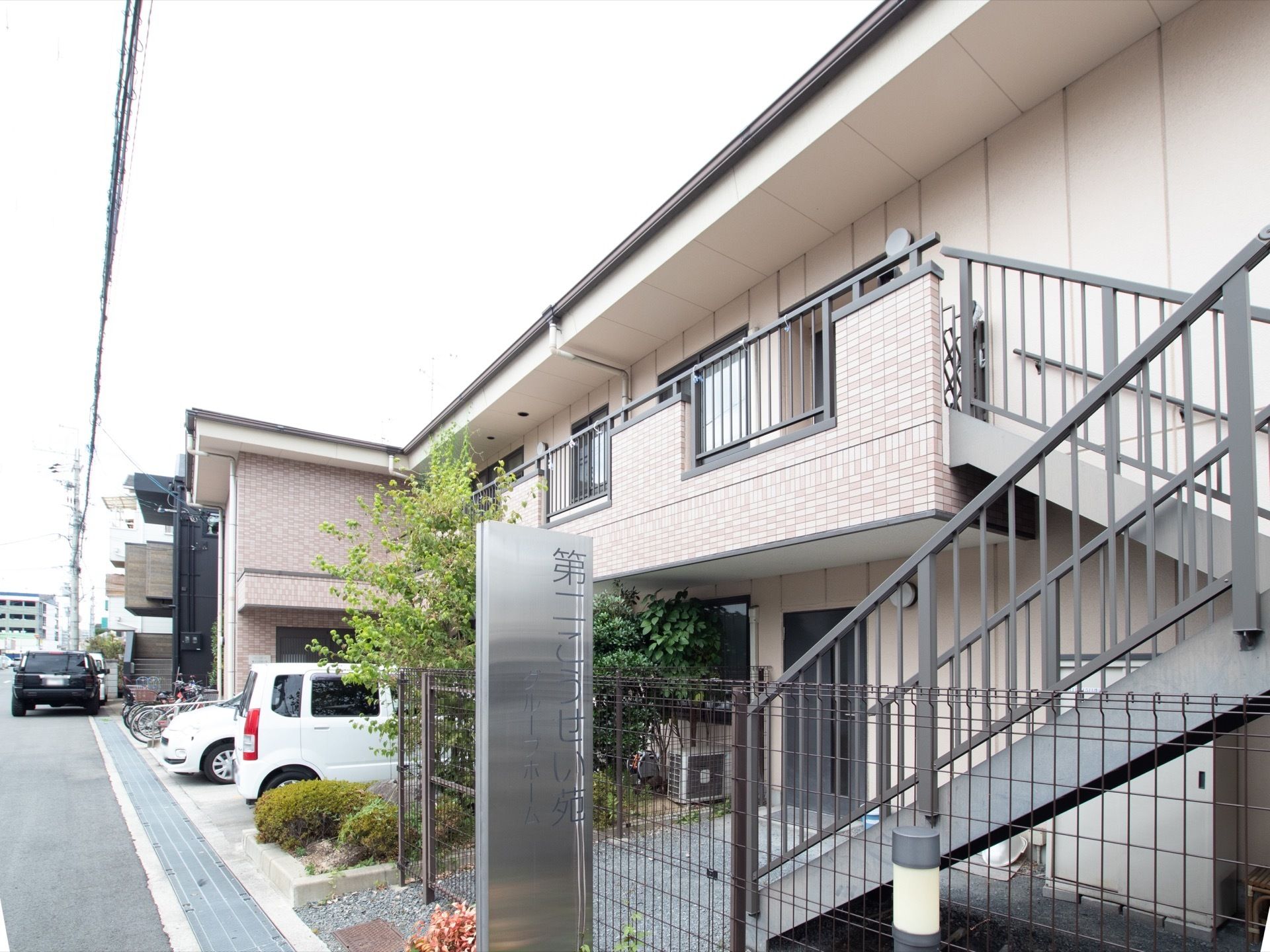 ２階建てのアパートのような建物である。２階に続く外階段が設けられている。建物前にはステンレス製の看板が掲げられている。