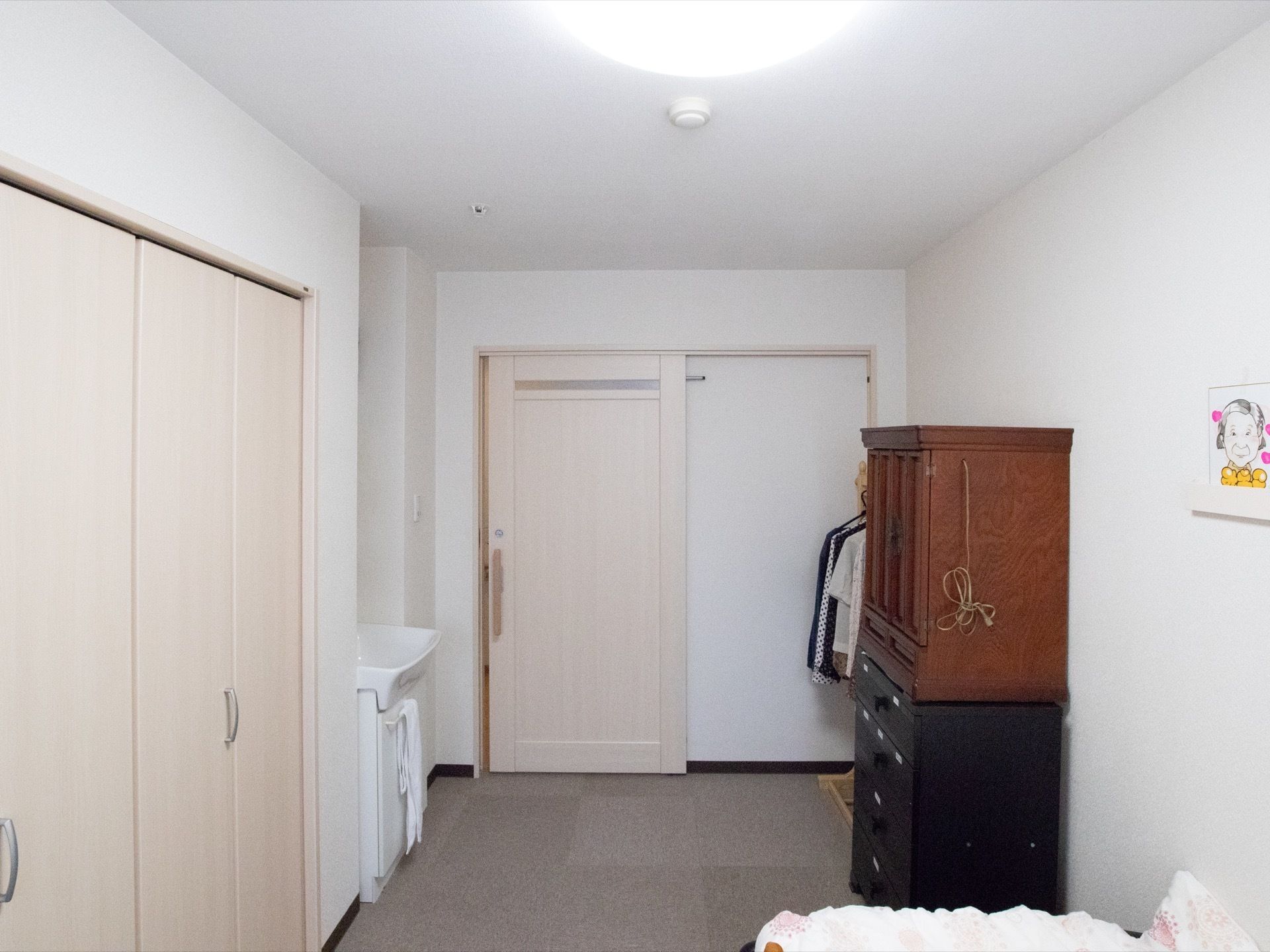 居室には洗面台が設けられている。居室ドアは大きく開くスライドドアを採用している。入居者様の私物である仏壇などが置かれている。