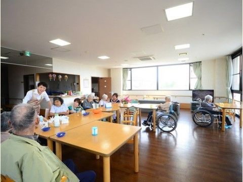 木製のテーブルセットの周りに集まってスタッフの話を聞く入居者様