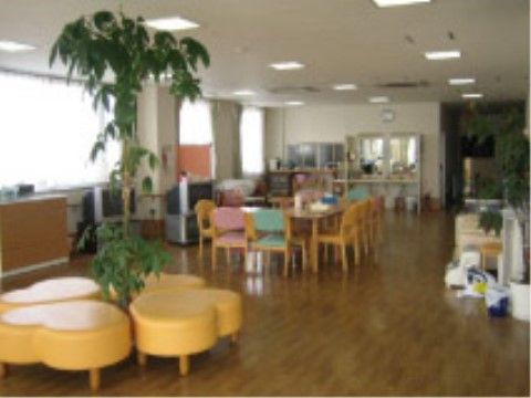 談話スペースには大きな窓があり、観葉植物が置かれている。フローリングの床には広いスペースが確保され、テーブルセットが設けられている。