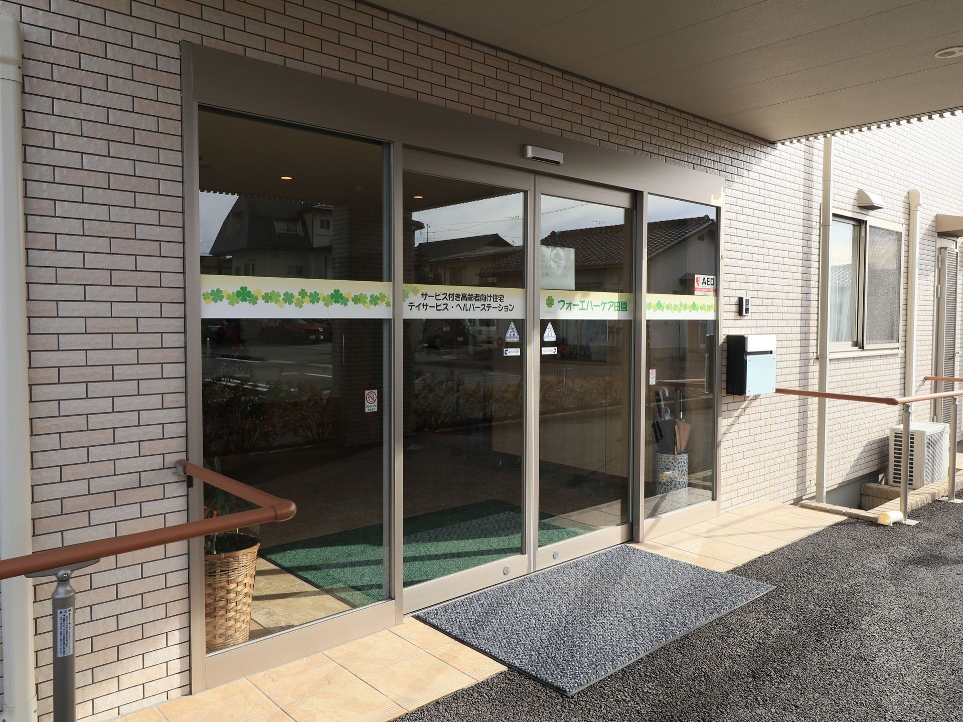扉には施設名が記されており、自動扉になっている。入り口にはマットが敷かれている。壁には手すりが備えつけられている。