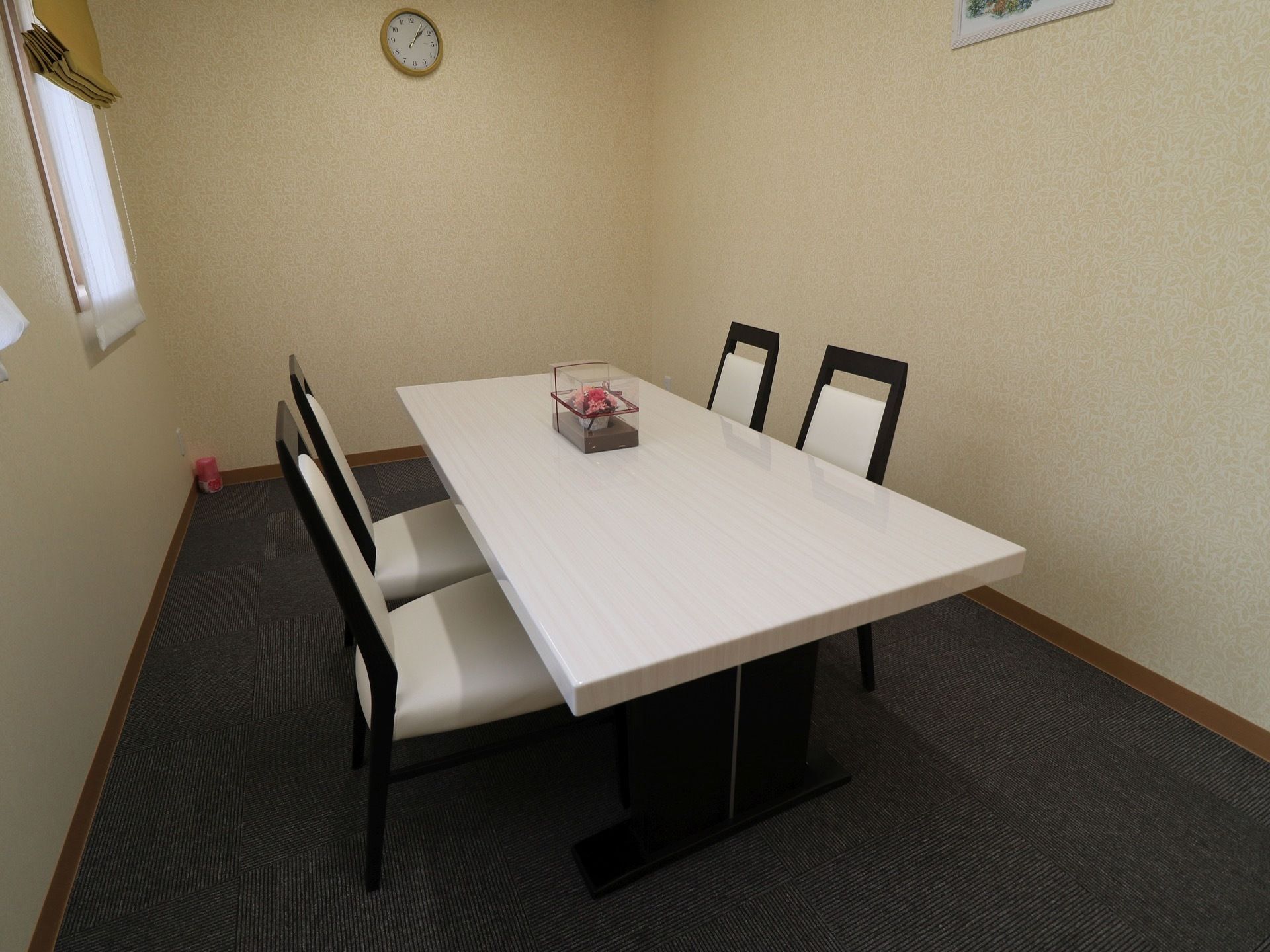 個室の部屋にテーブルと椅子が用意されている。テーブルの上には小物が設置されている。壁には時計と絵が飾られている。