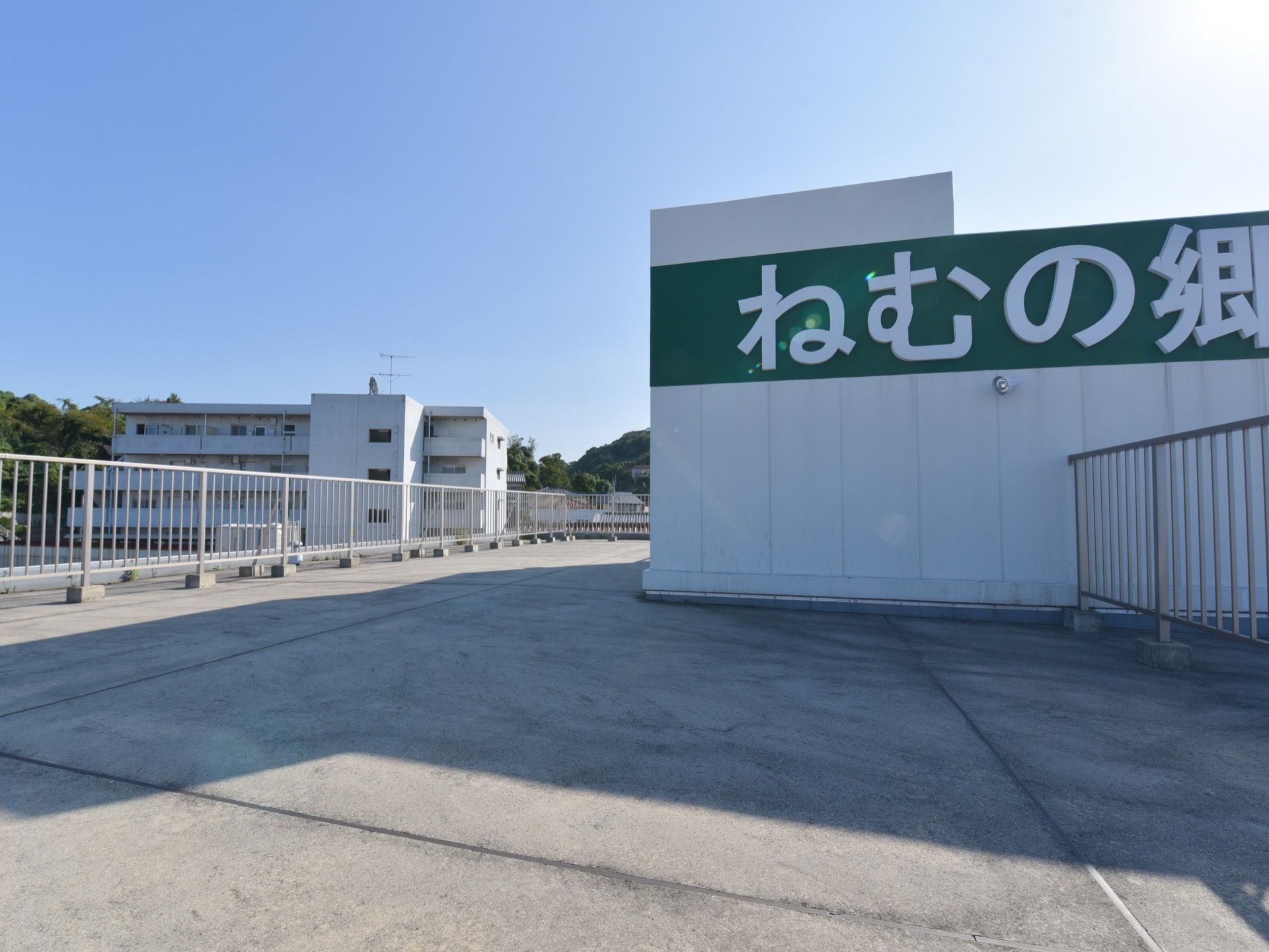 とても広い屋上で、周りに背の高いフェンスが取り付けられている。右側には施設名が書かれた大きな看板がある。