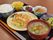 ご飯やみそ汁、野菜中心の主菜や副菜が黒いトレイに並べられている。箸も置かれており、食後のデザートも用意されている。