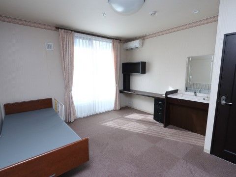 木製の介護用ベッドや洗面台、作り付けのデスクがある居室