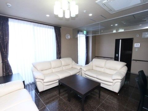 居室前の広々としたスペースに、白い大きなソファーが３つと机が置かれている。大きな窓からは日が入り、とても室内が明るい。