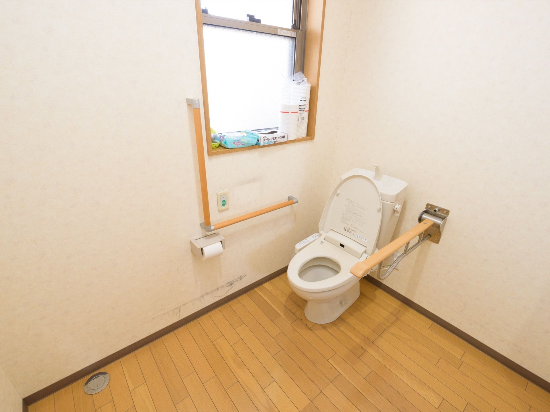広々としたスペースのトイレである。横側には上げ下げ式の窓がある。壁際には、エル型の手すりとナースコールを取り付けている。