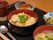 親子丼と味噌汁に小鉢を１品、それにデザートにプリンを添えている。手前にお箸とスプーンを置き、横側には、お茶もある。