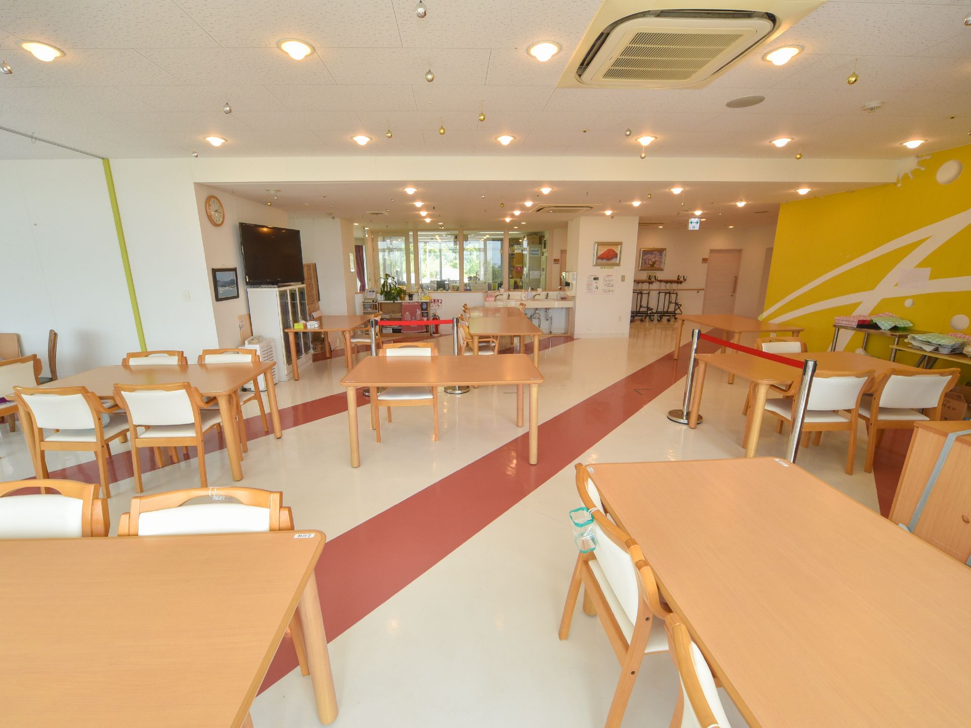 明るく広々とした食堂。天井にエアコンが設置されている。テレビや時計も置かれている。食堂内をポールで区切っている。