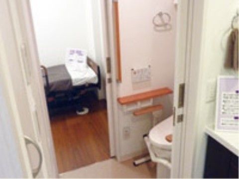 引き戸の入口が開けられたトイレと、その奥にある茶色のベッド