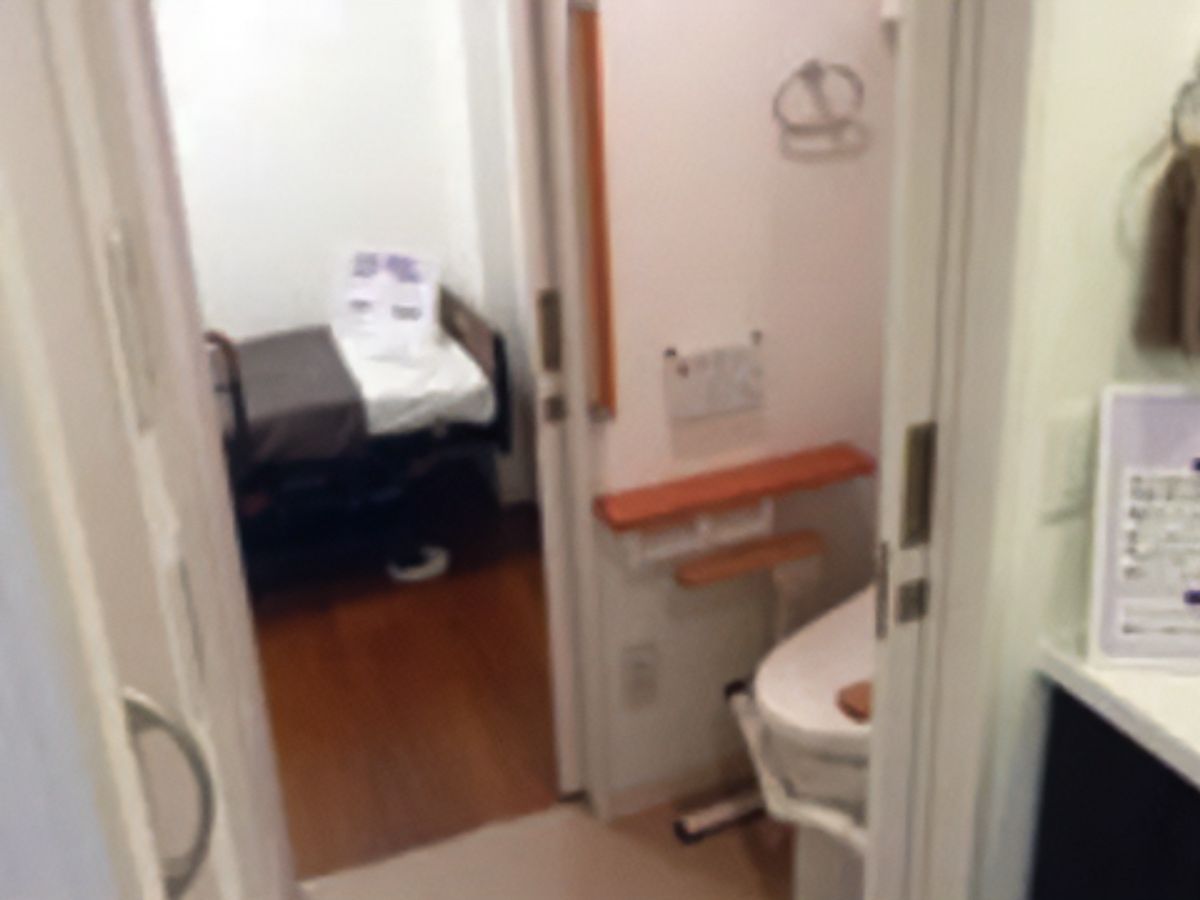 引き戸の入口が開けられたトイレと、その奥にある茶色のベッド