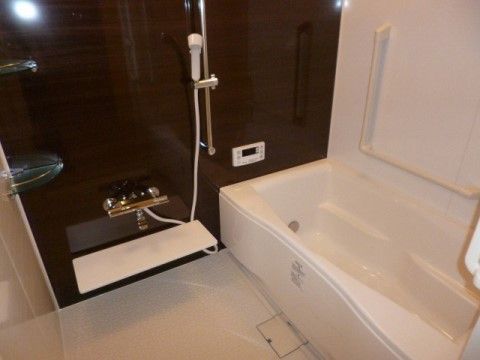 浴室の洗い場にはコーナーラック、蛇口の下には白い棚がある。浴槽の壁側にはL字型の手すりが取り付けられている。