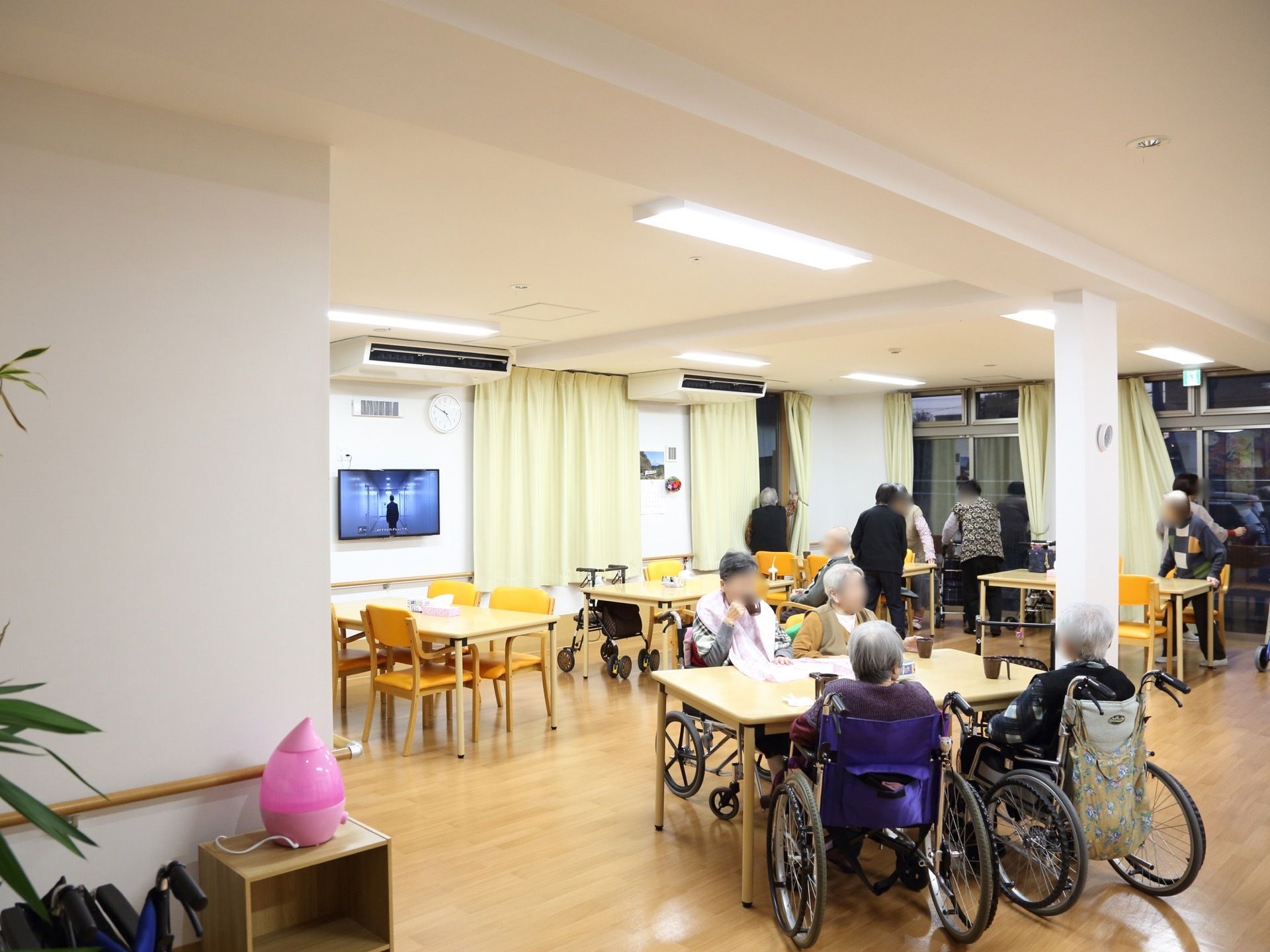 壁掛けテレビが、食堂の左側に設置されている。その横には大きな窓があり、ペールグリーンのカーテンが掛けてある。