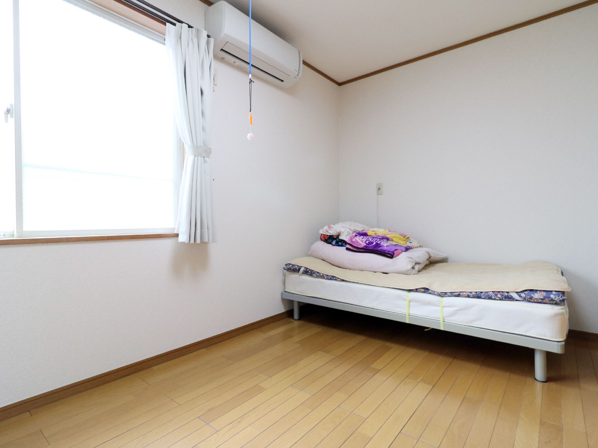白いマットレスやカラフルな柄のタオルなどが畳まれたベッドの置かれた部屋