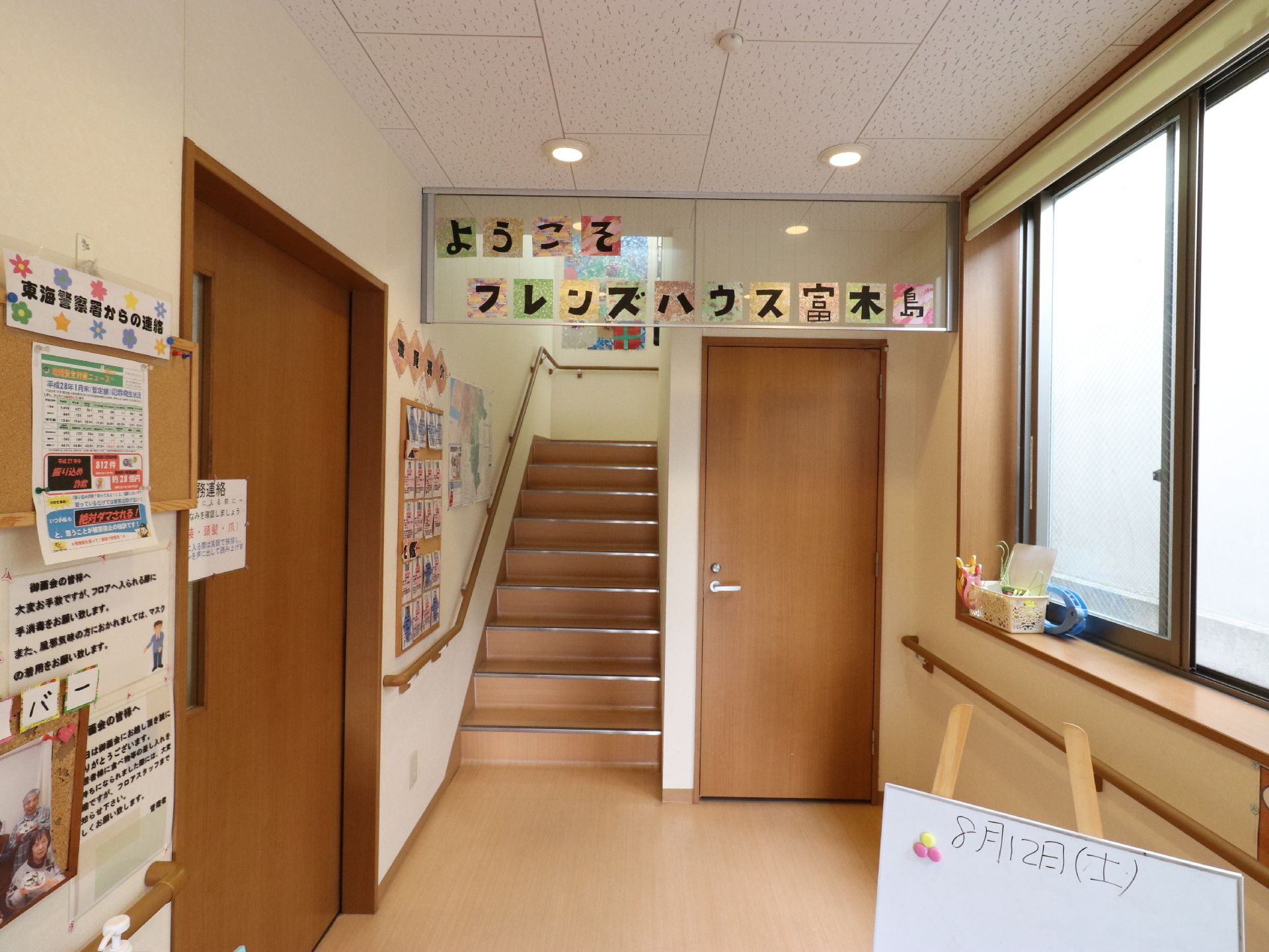 壁に手摺が設置されている。奥に階段と木の扉があり、その上に手作りでつくられた歓迎の言葉が飾られている。