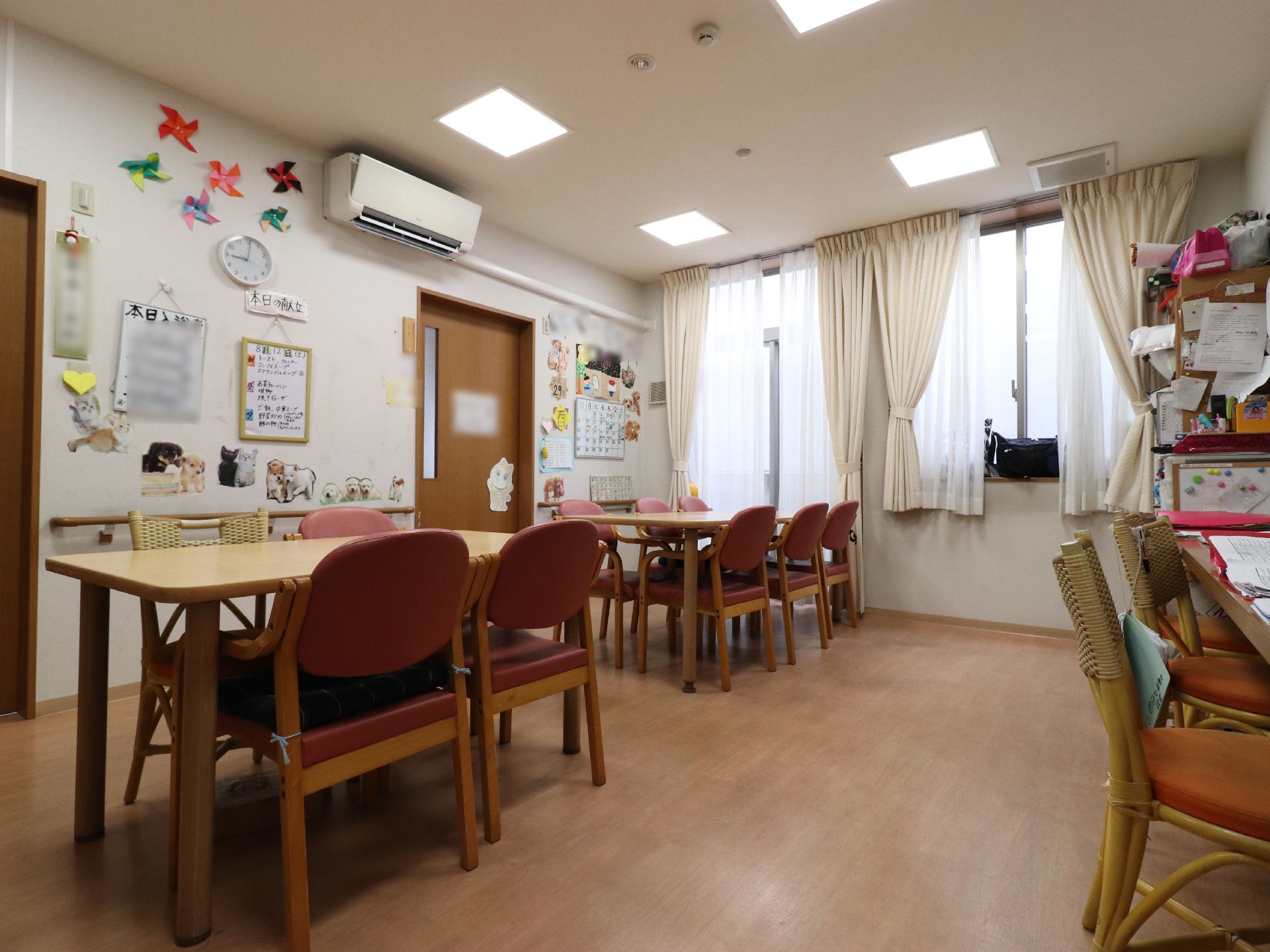 たくさんのテーブルやイスがある部屋には、壁際に「本日の献立」や「本日の入浴者」などの情報が記されている紙が数多く貼られている。
