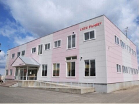 白と淡いピンクのストライプに塗られた２階建ての建物。玄関前には階段があり、横には傾斜の緩やかなスロープがある。