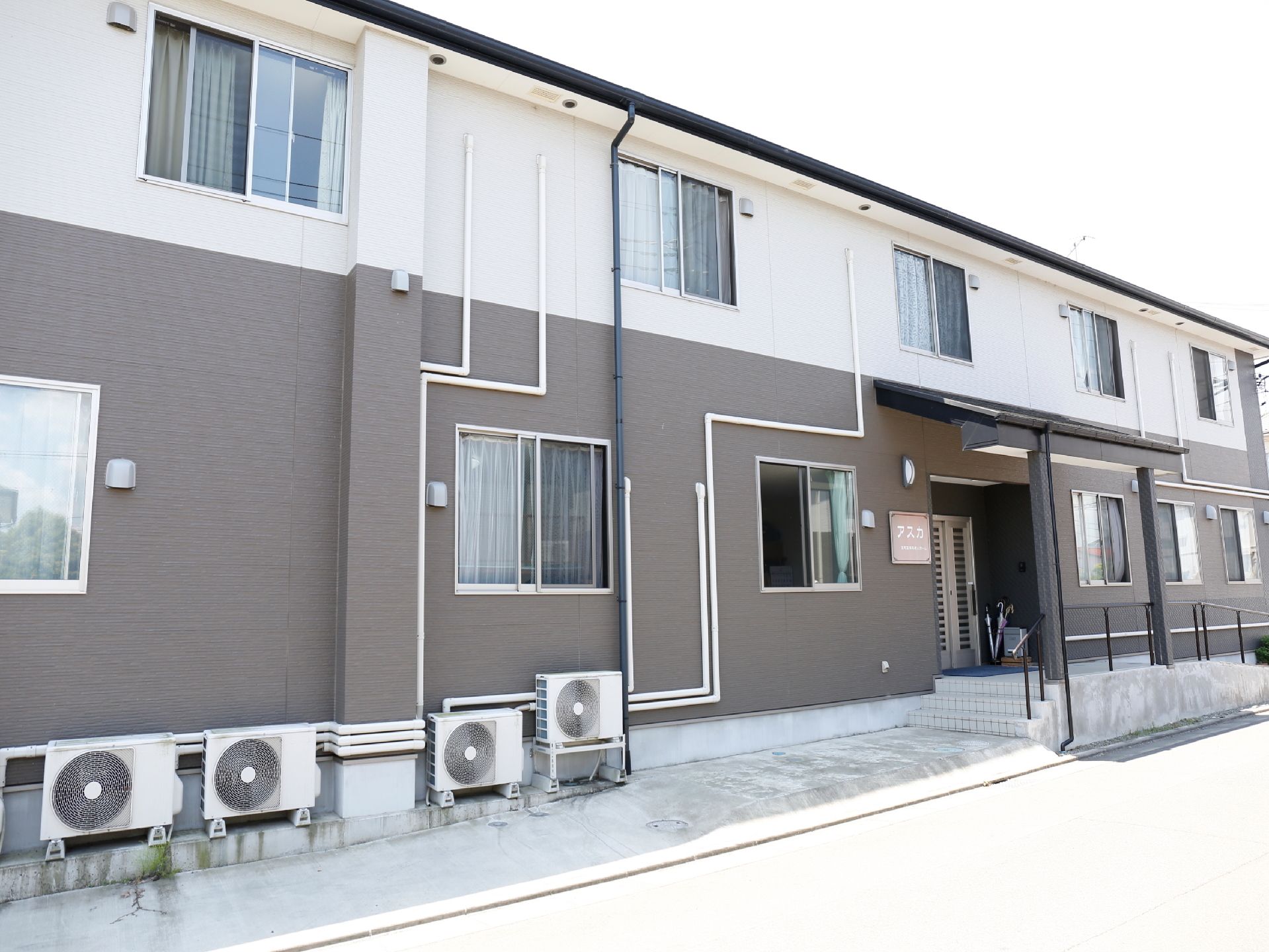 住宅型有料老人ホームの外壁にはホワイトとブラウンが配色されている。また施設の建物は2階建てとなっている。