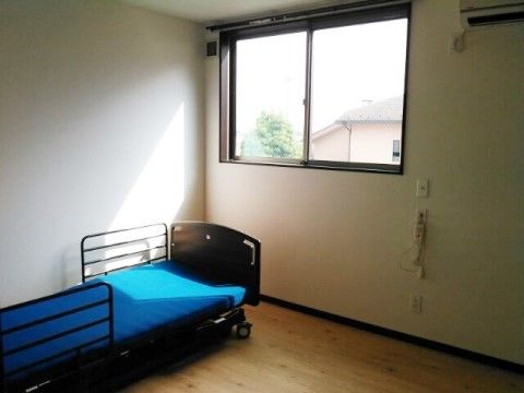 青いマットレスの介護用ベッドに外光差し込んでいる居室