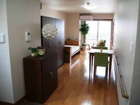 エアコンが完備された個室である。壁に手すりやインターホンモニターが設置されている。ベランダへと続く窓がある。