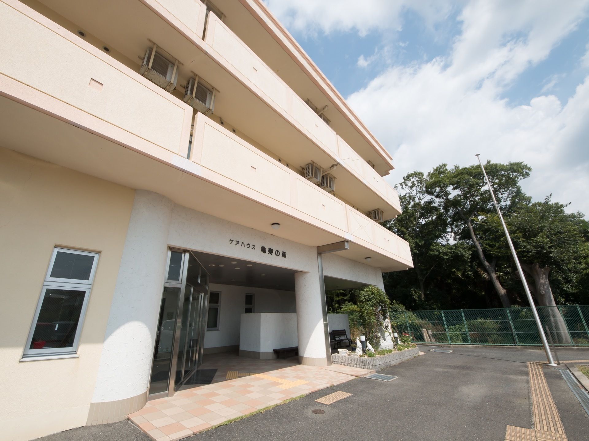 施設建物の玄関付近の外観。ピロティ構造になっている自動ドアの前の床には、目の不自由な方のための点字ブロックがある。
