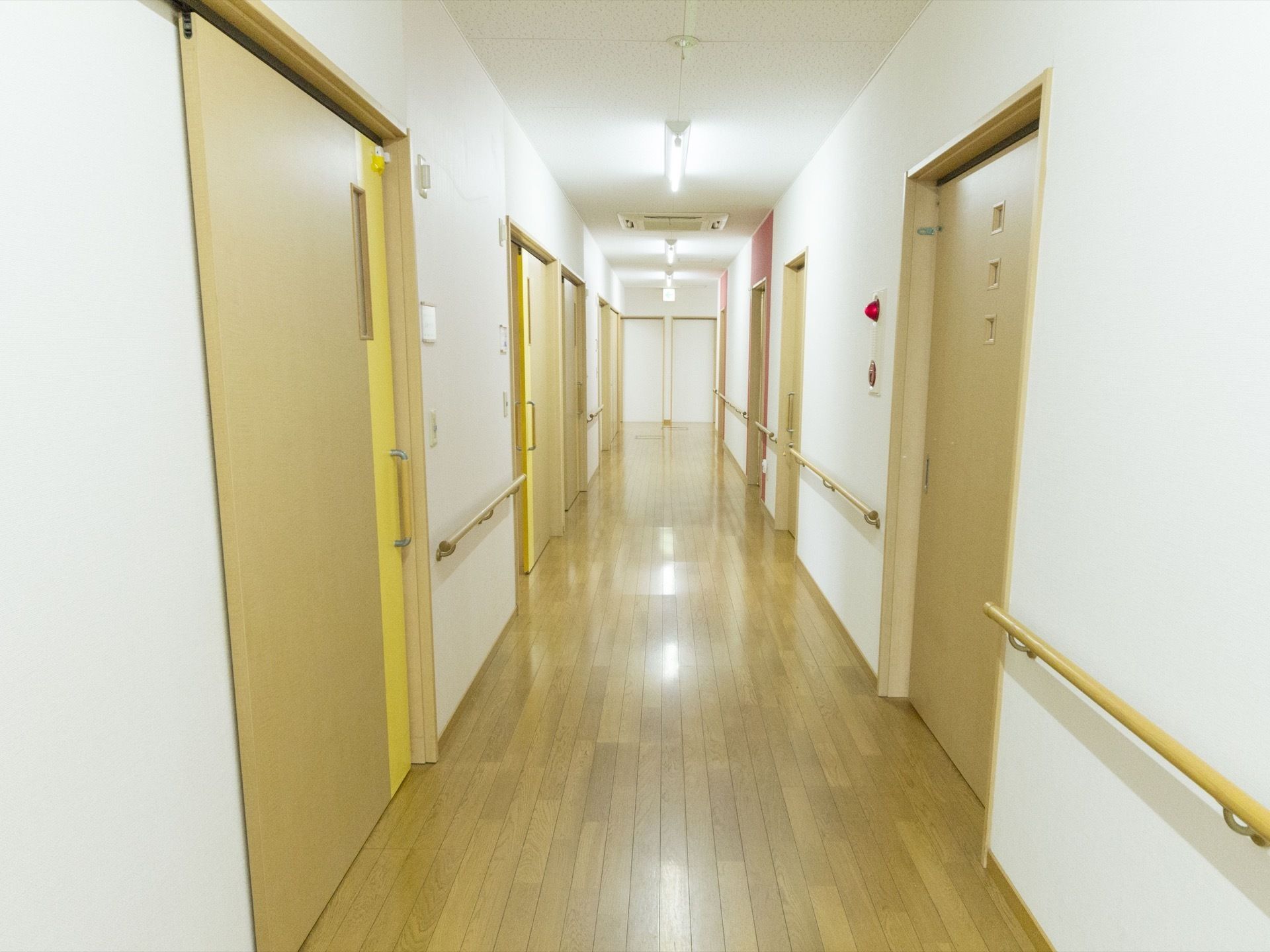 廊下の床は、木の板が敷かれたフローリングである。白色の壁に、木製のドアが並んでいる。壁には手すりが付いている。