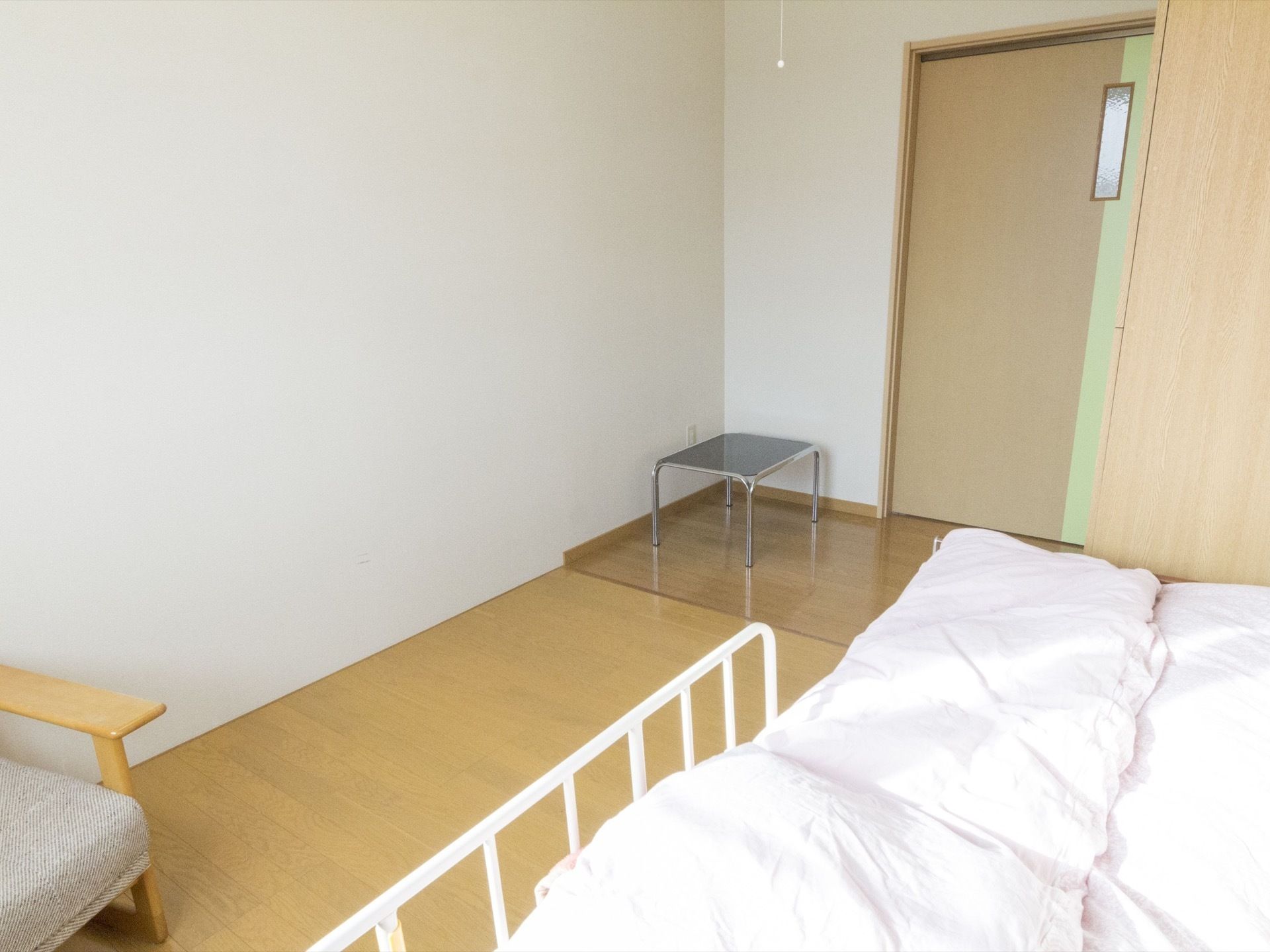 部屋の奥から見た居室の様子。右手にベッドが置かれていて、左手に椅子がある。部屋の入口にも椅子が置かれている。