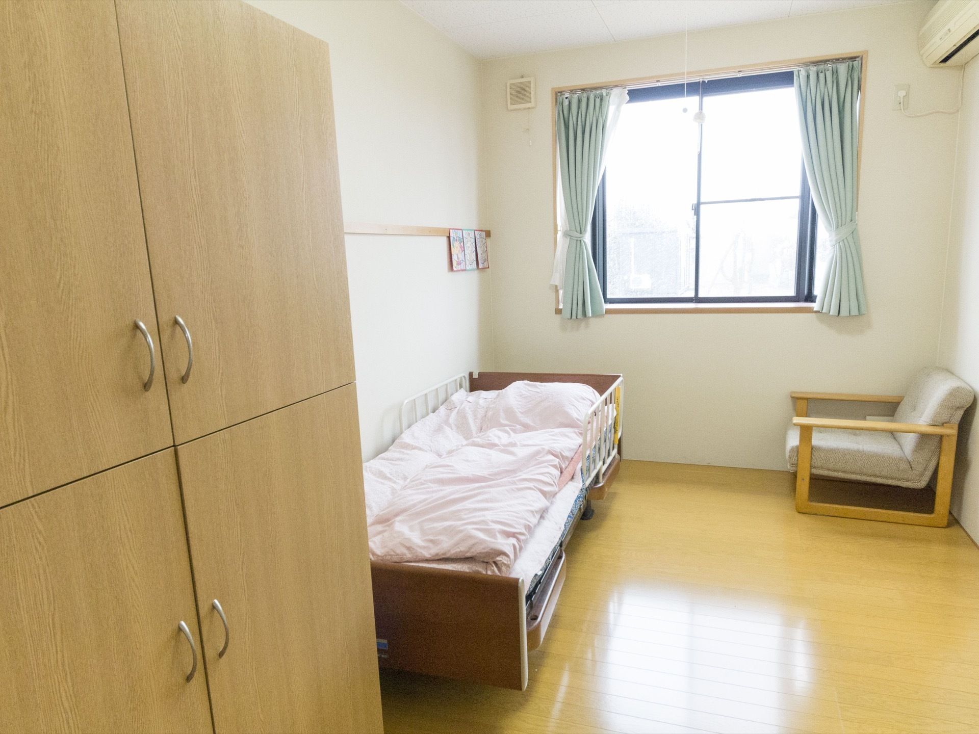部屋の左手に、木製のクローゼットがある。部屋の奥に窓があり、カーテンが付いている。その前にベッドが置かれている。