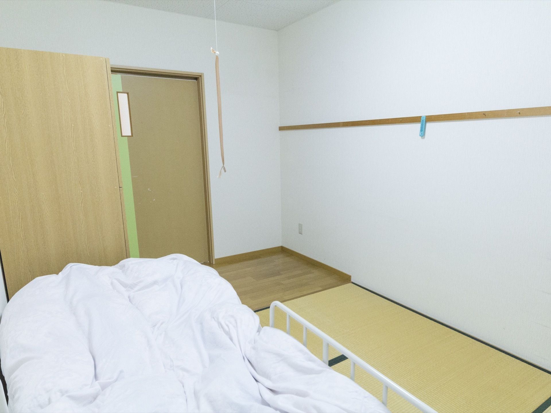 部屋の左側にベッドが置かれ、掛け布団が敷かれている。ベッドの横には、畳が数枚敷いてある。部屋の入口にはフローリングの部分が見える。