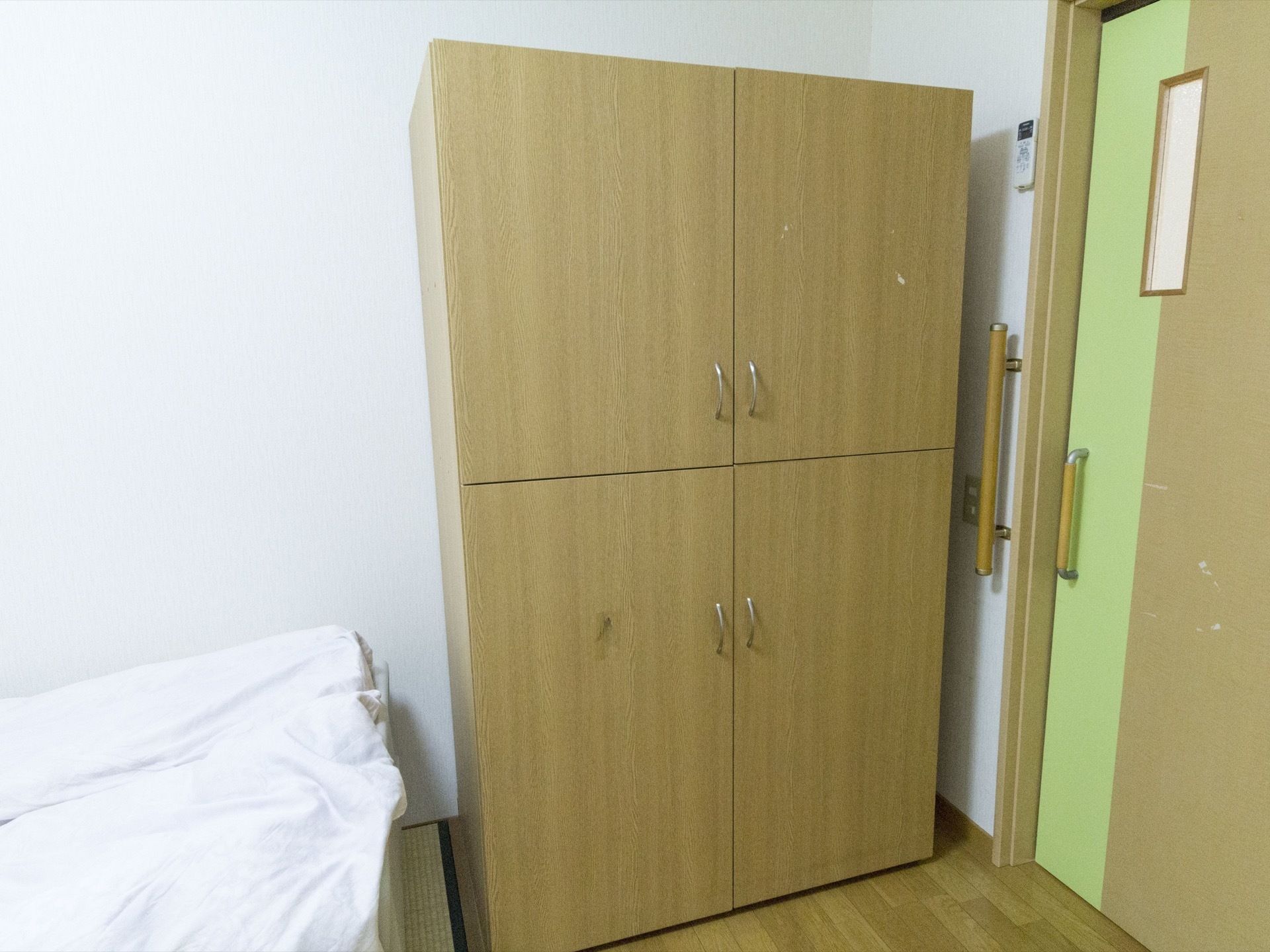 居室入口のドアは横開きで、木製の扉に黄緑色の線が入っている。入口のすぐ近くに、２段に分かれて観音扉の付いたクローゼットが置かれている。