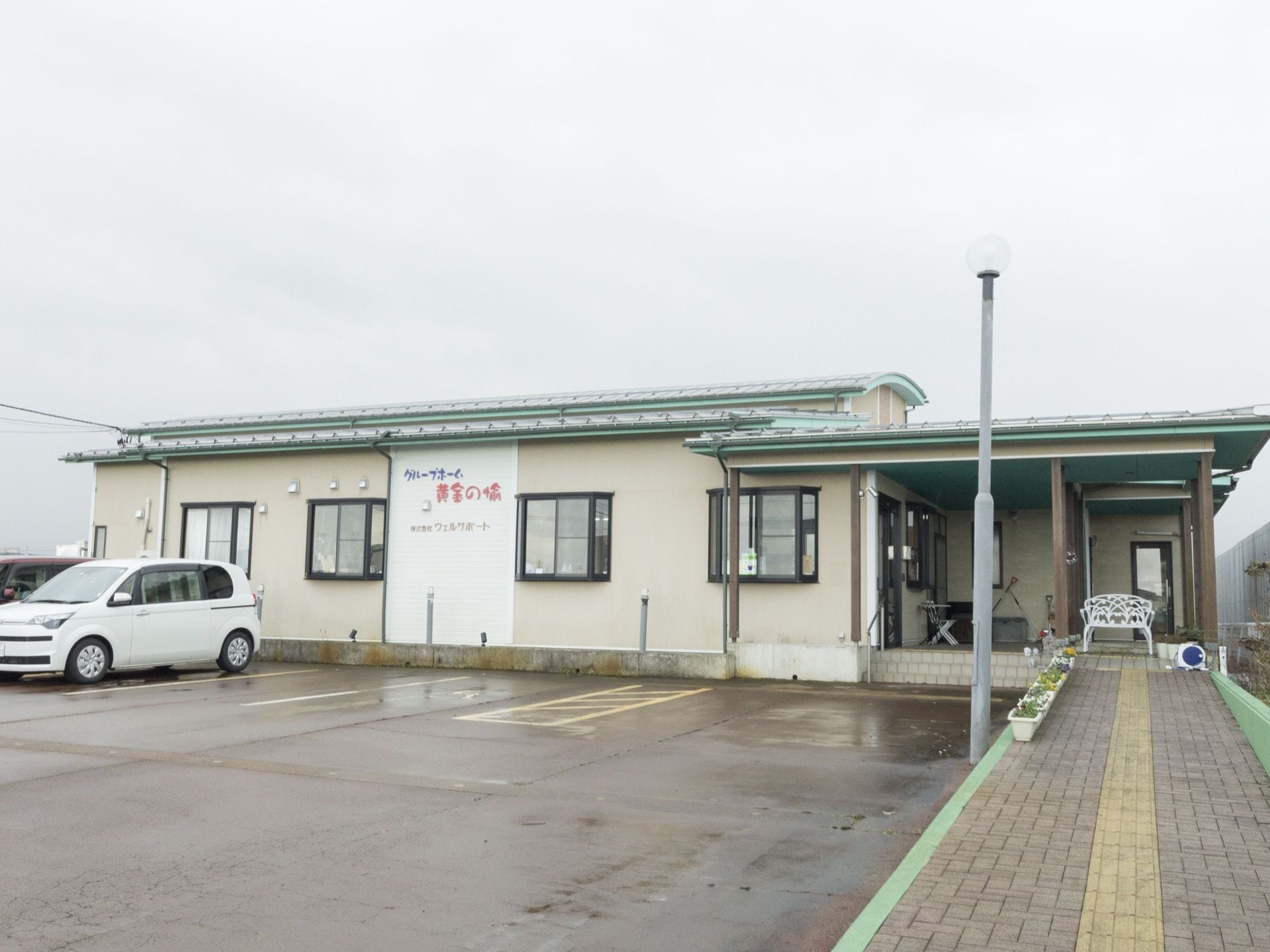 建物の外壁に、施設名と会社名が表示されている。壁の色はベージュ色で、屋根の下は緑色をしている。壁には出窓が付いている。