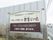 敷地の入口にある、施設の看板。鉄製の看板に、施設名が表示されている。看板の後ろには、鉄板が設置されている。