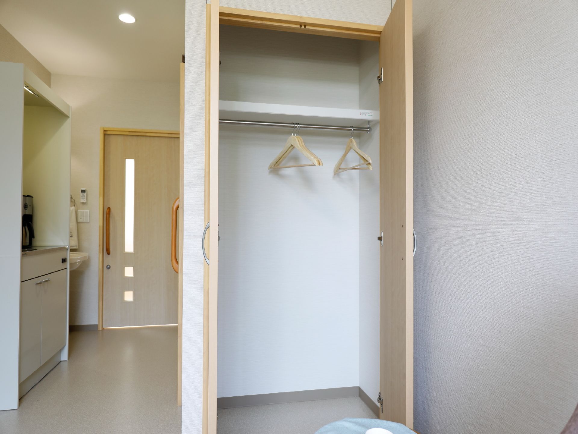 個室に設置された収納スペースである。内部は白色の壁とグレーの床で、洋服を掛けれ、上部には、小物を置いたりできる棚がある。