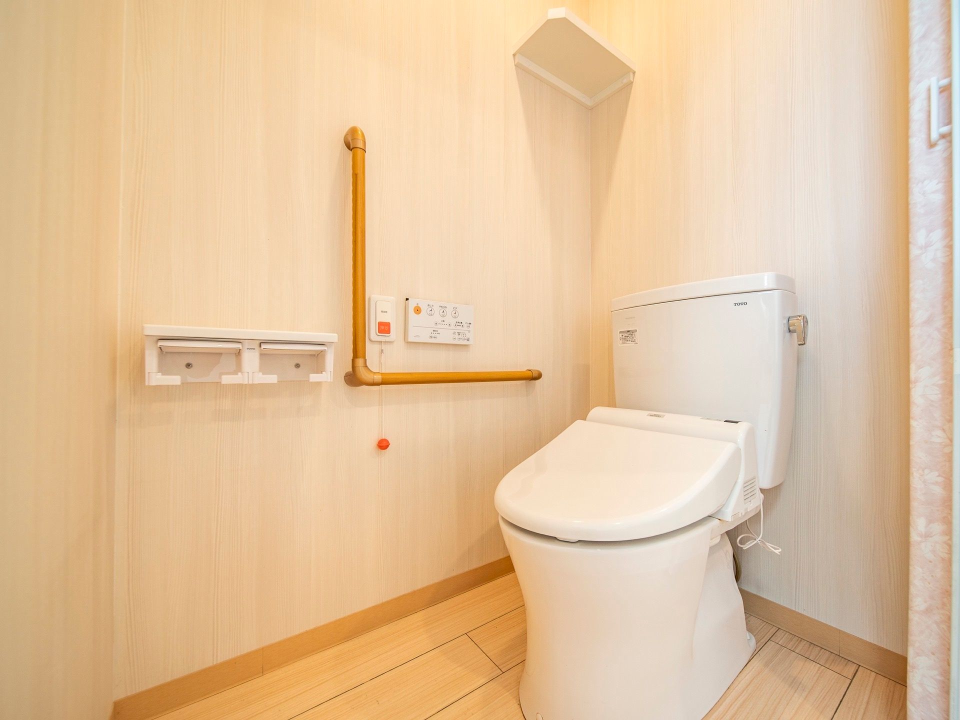 洗浄暖房機能つきのトイレが設置されている。操作パネルの左側に、オレンジ色の緊急呼び出しボタンがついている。